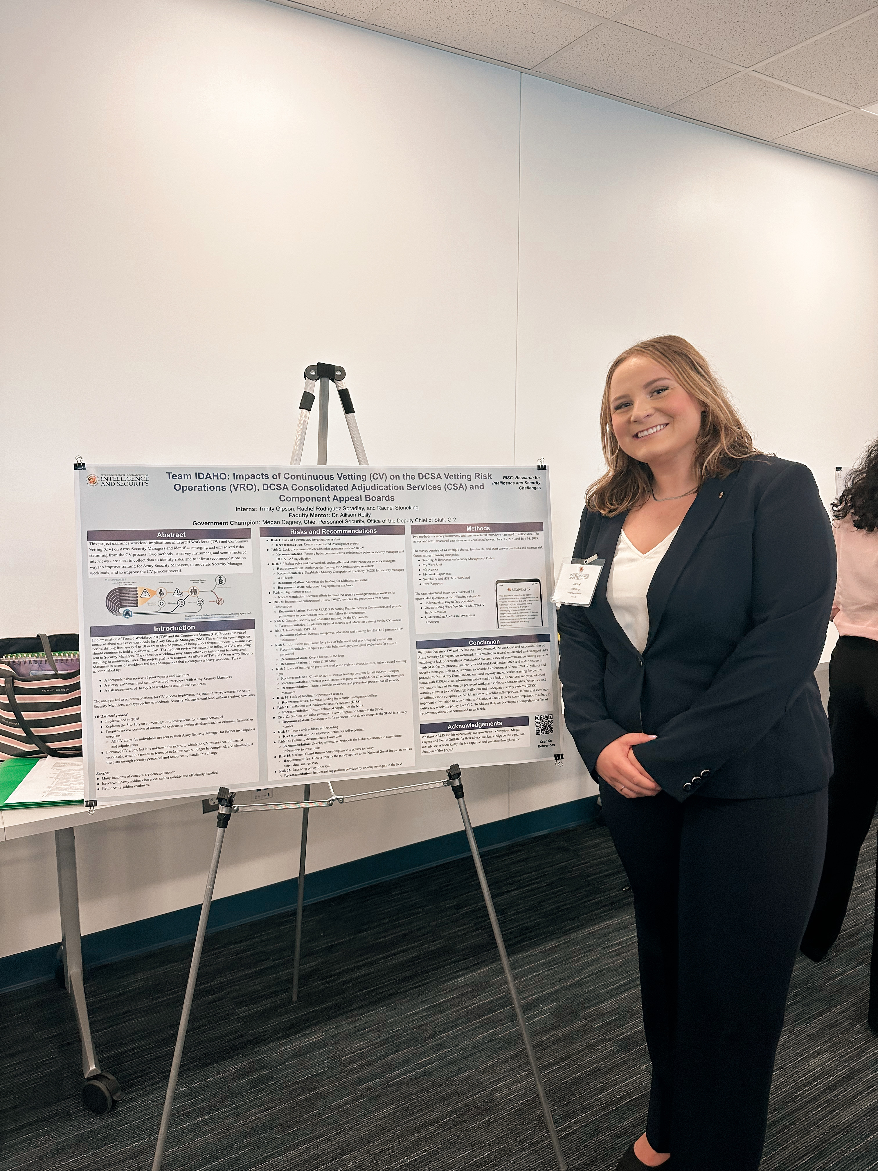 Female intern stands proudly next to research presentation on a tripod