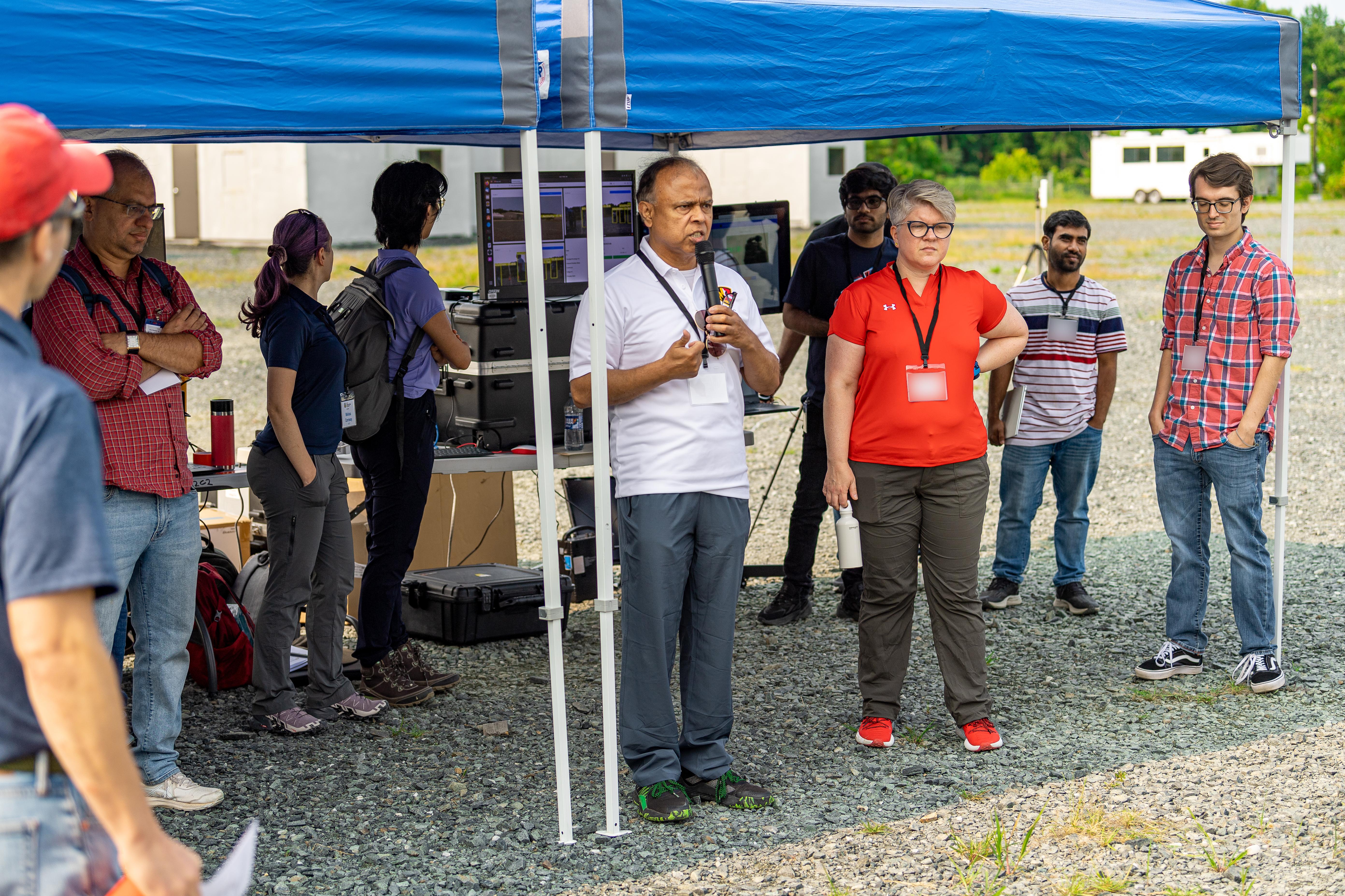ArtIAMAS researcher speaks outside under a canopy surrounded by students and colleagues